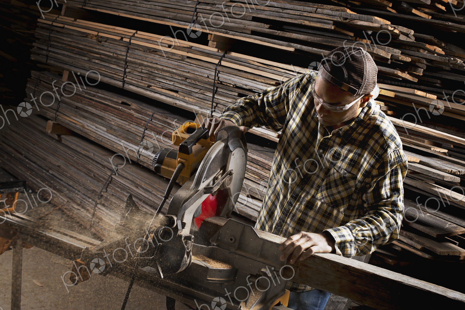 A reclaimed lumber workshop. A man in protective eye goggles using a circular saw to…
