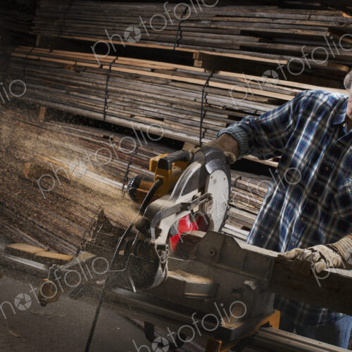 A reclaimed lumber workshop. A man in protective eye goggles using a circular saw to…