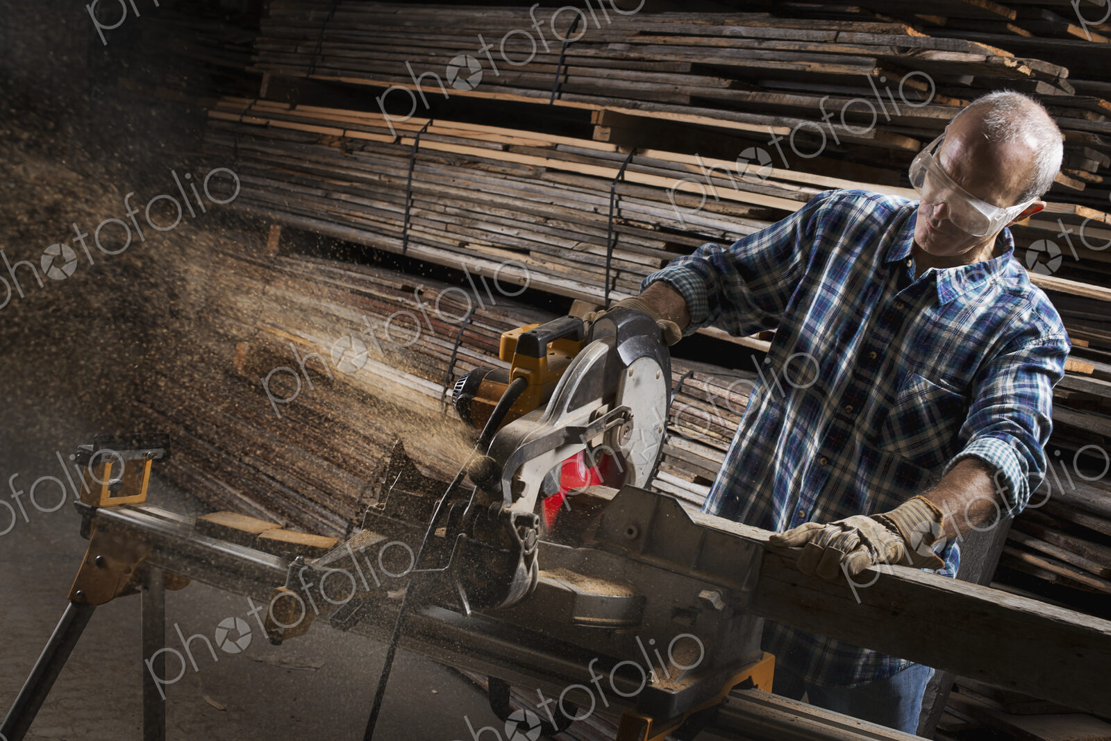 A reclaimed lumber workshop. A man in protective eye goggles using a circular saw to…