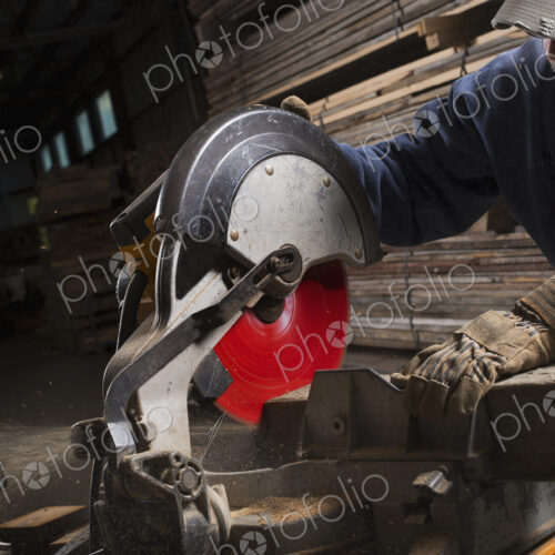 A reclaimed lumber workshop. A man in protective eye goggles using a circular saw to…
