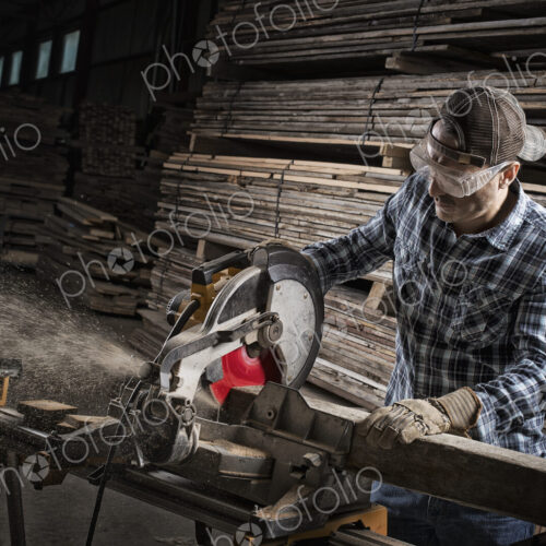 A reclaimed lumber workshop. A man in protective eye goggles using a circular saw to…