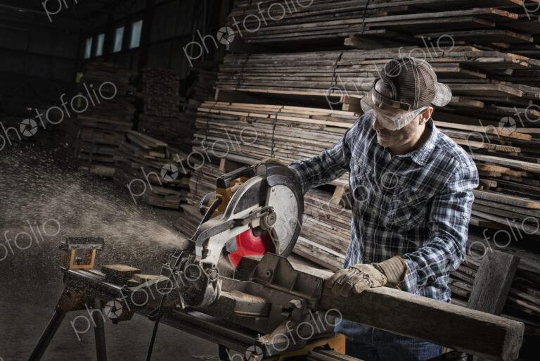 A reclaimed lumber workshop. A man in protective eye goggles using a circular saw to…