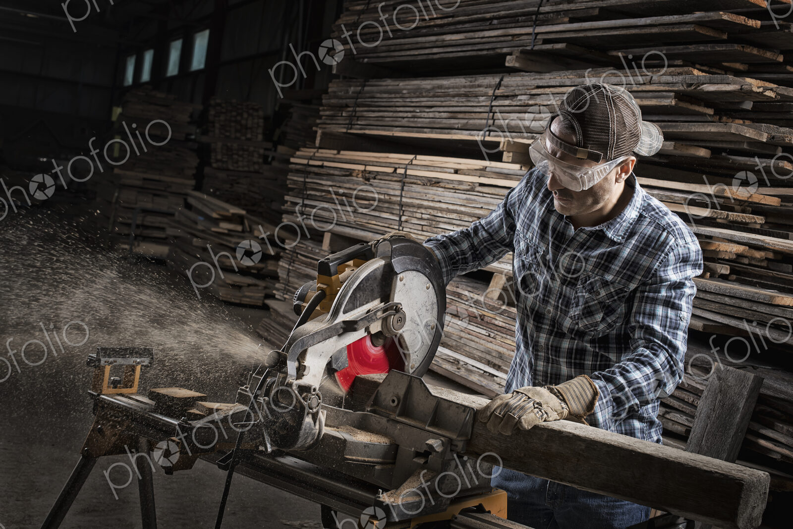 A reclaimed lumber workshop. A man in protective eye goggles using a circular saw to…