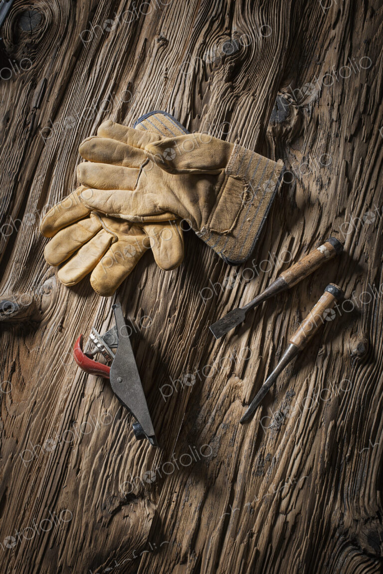 A reclaimed lumber yard workshop. A pair of leather working gloves, and handheld…