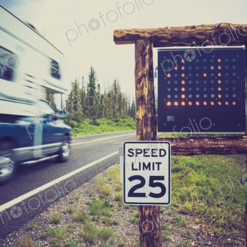 A recreational vehicle drives past a 25 mph limit sign and radar display on a forested… A recreational vehicle drives past a 25 mph limit sign and radar display on a forested…