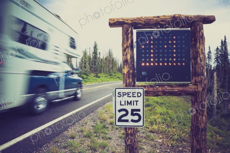 A recreational vehicle drives past a 25 mph limit sign and radar display on a forested…