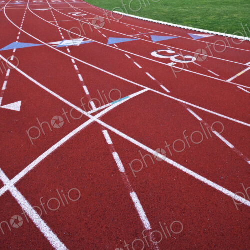 A red artificial surface running track. A sports ground. Painted marked lines for lanes.