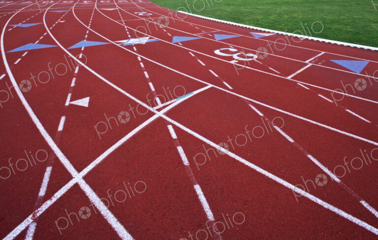 A red artificial surface running track. A sports ground. Painted marked lines for lanes.