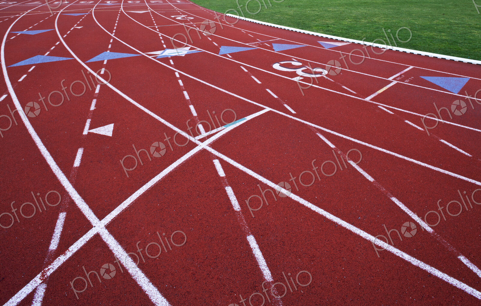 A red artificial surface running track. A sports ground. Painted marked lines for lanes.