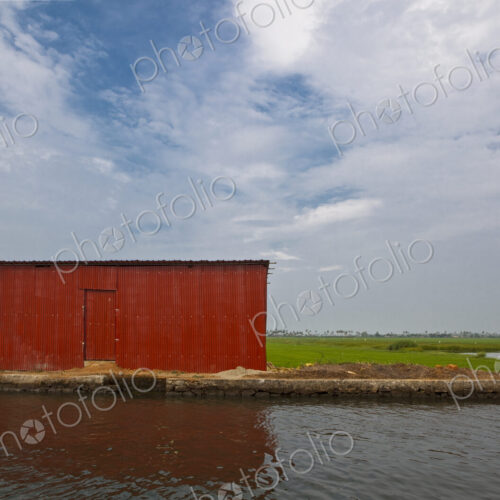A red barn on the water's edge on a waterway in the Kerala region near Alleppey, the… A red barn on the water's edge on a waterway in the Kerala region near Alleppey, the…