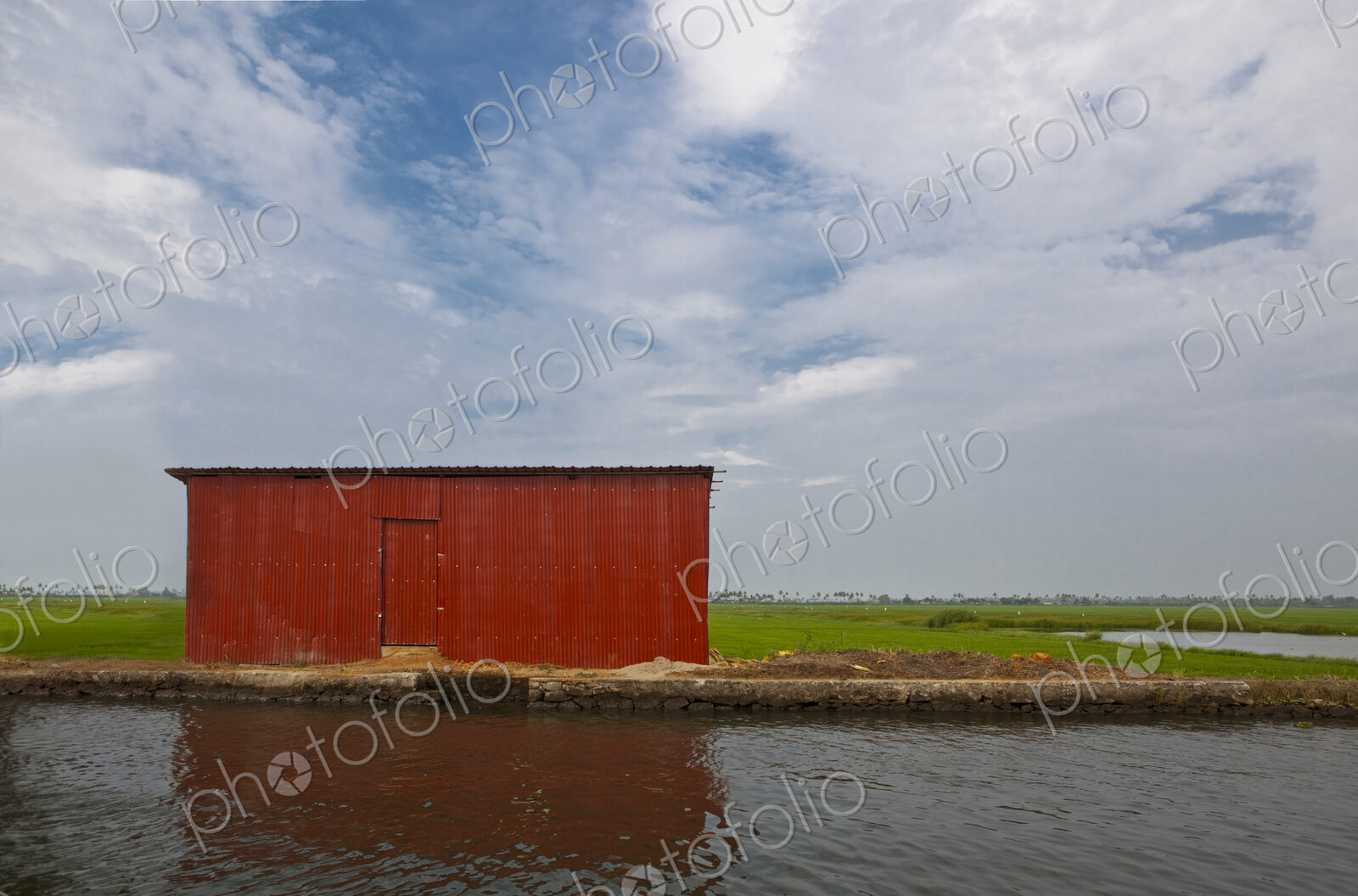 A red barn on the water’s edge on a waterway in the Kerala region near Alleppey, the…
