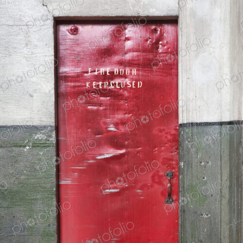 A red barrier fire door in a museum, notice Fire Door Keep Closed, dents and marks on…