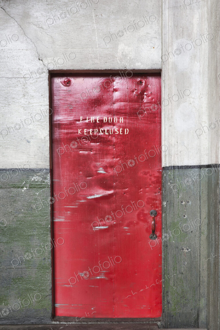 A red barrier fire door in a museum, notice Fire Door Keep Closed, dents and marks on…