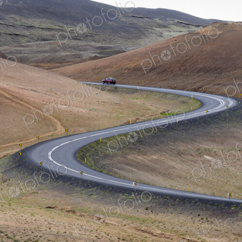 A red car on a winding road through the mountains.