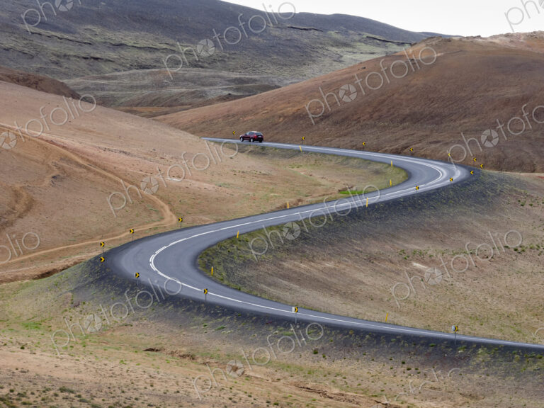 A red car on a winding road through the mountains.