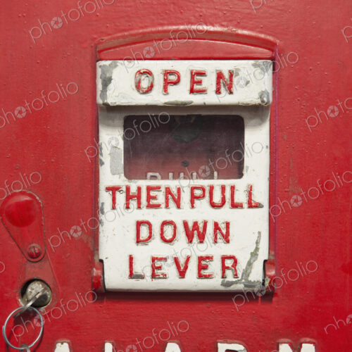 A red metal historic antique fire alarm box. An alarm lever with written instruction A red metal historic antique fire alarm box. An alarm lever with written instruction