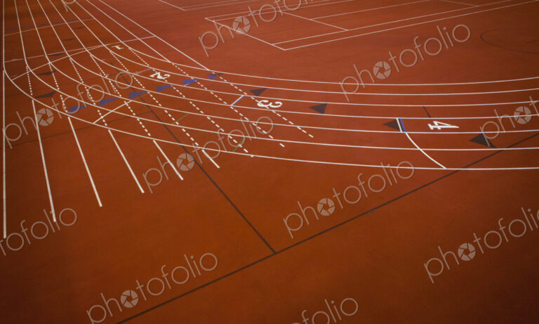 A red running track, athletics ground, a corner section of track marked with lanes