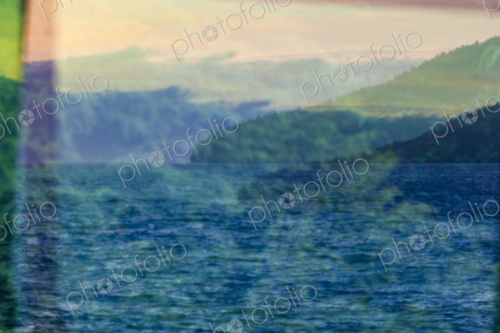 A reflection in window glass of the forest, mountains and moving water.
