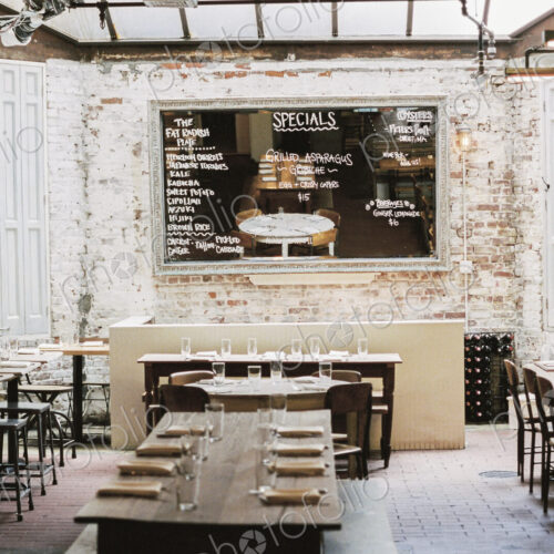A restaurant with long narrow tables and chairs laid for a meal. A large chalk menu board. A restaurant with long narrow tables and chairs laid for a meal. A large chalk menu board.