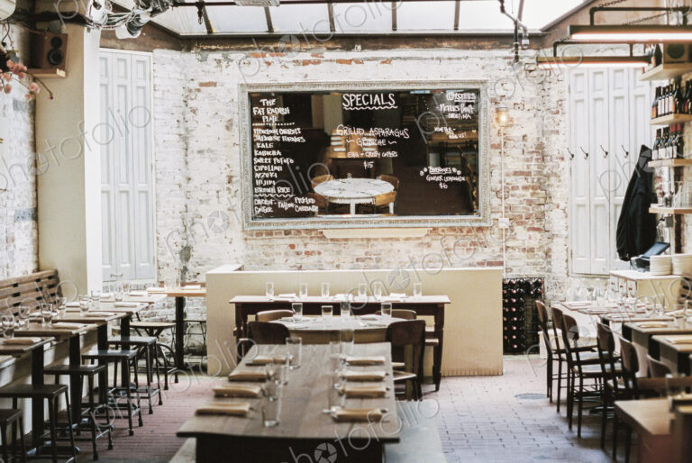 A restaurant with long narrow tables and chairs laid for a meal. A large chalk menu board.