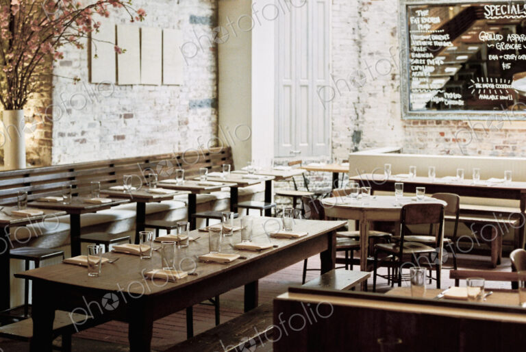 A restaurant with long narrow tables and chairs laid for a meal. A large chalk menu board.