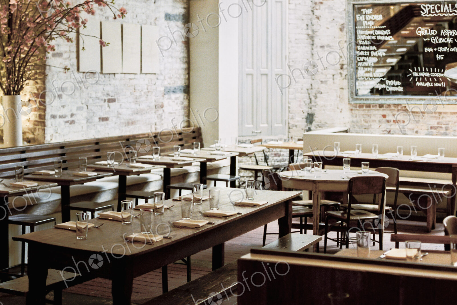 A restaurant with long narrow tables and chairs laid for a meal. A large chalk menu board.