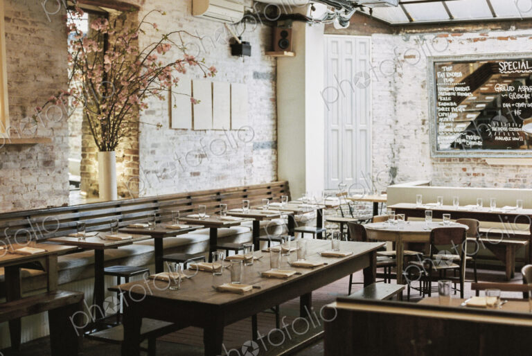 A restaurant with long narrow tables and chairs laid for a meal. A large chalk menu board.