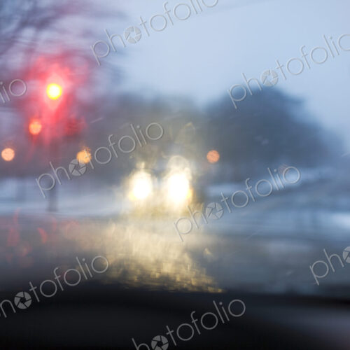 A road in bad weather view through a car windscreen, traffic lights on red, rain on…