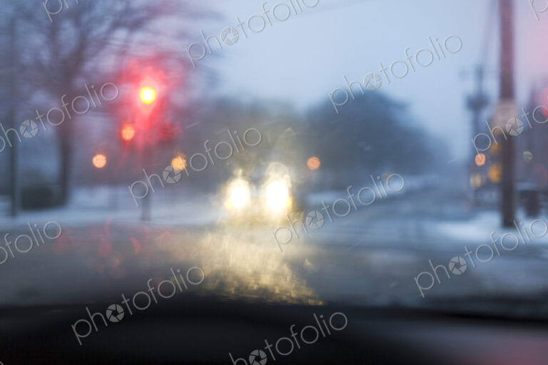 A road in bad weather view through a car windscreen, traffic lights on red, rain on…