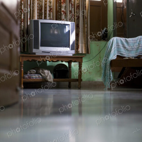 A room interior with television on a small table, curtains and bed.