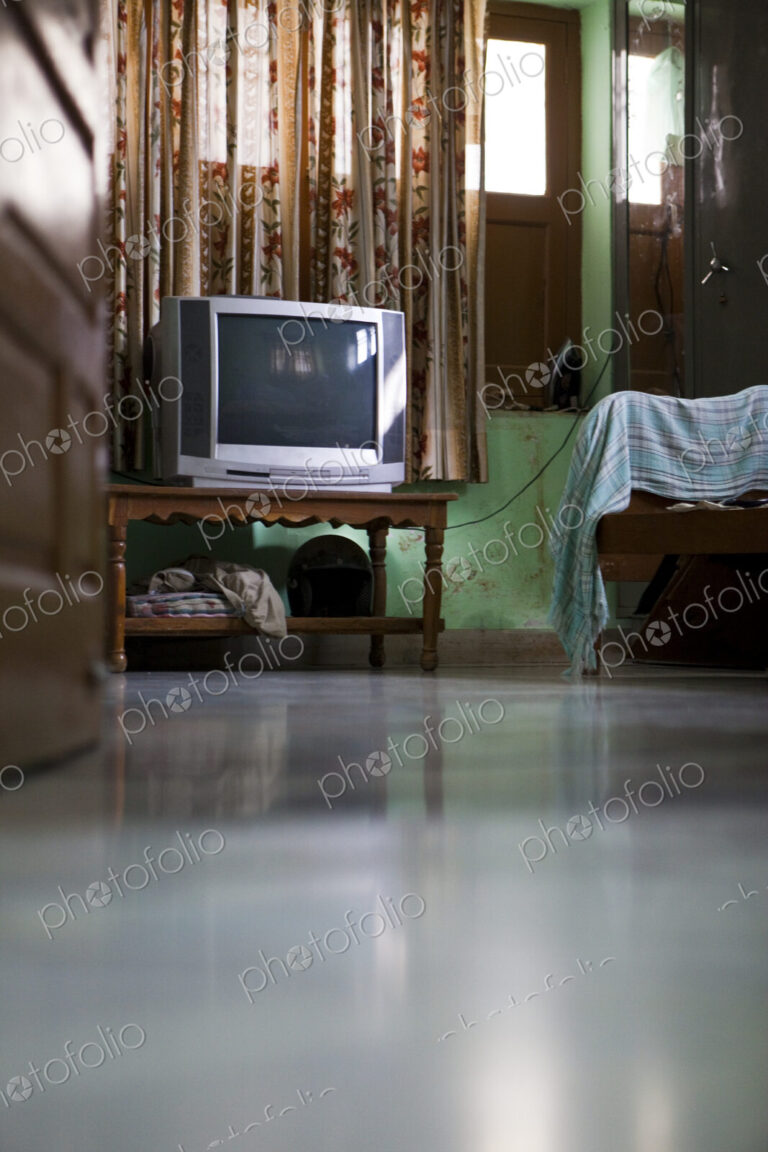 A room interior with television on a small table, curtains and bed.