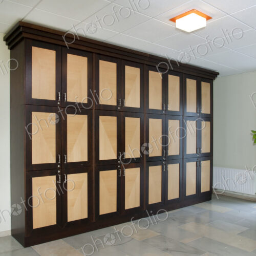 A room with a row of lockers with handles, storage, a tiled floor and ceiling light. A room with a row of lockers with handles, storage, a tiled floor and ceiling light.