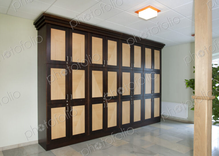 A room with a row of lockers with handles, storage, a tiled floor and ceiling light.