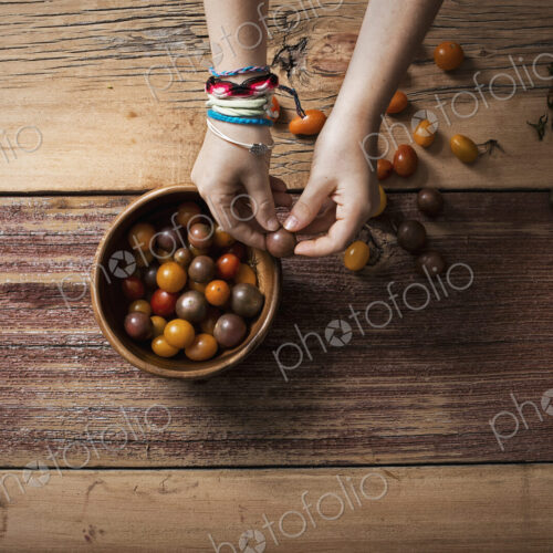 A round bowl with small tomatoes of various colours, and a person sorting and picking…