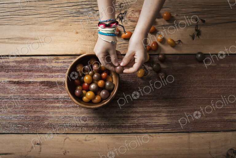 A round bowl with small tomatoes of various colours, and a person sorting and picking…