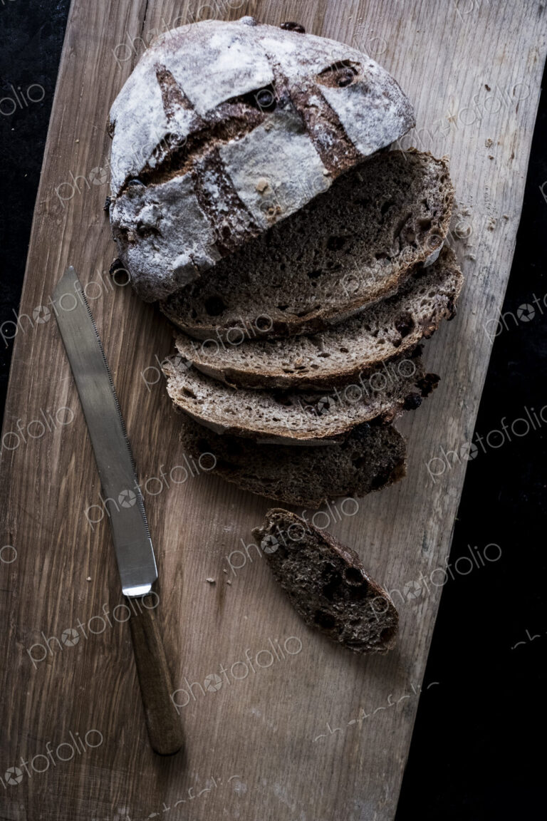 A round loaf of brown bread on a bread board partly sliced.
