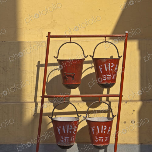 A row of red fire sand buckets on a frame outside a building, the Birla temple in New… A row of red fire sand buckets on a frame outside a building, the Birla temple in New…