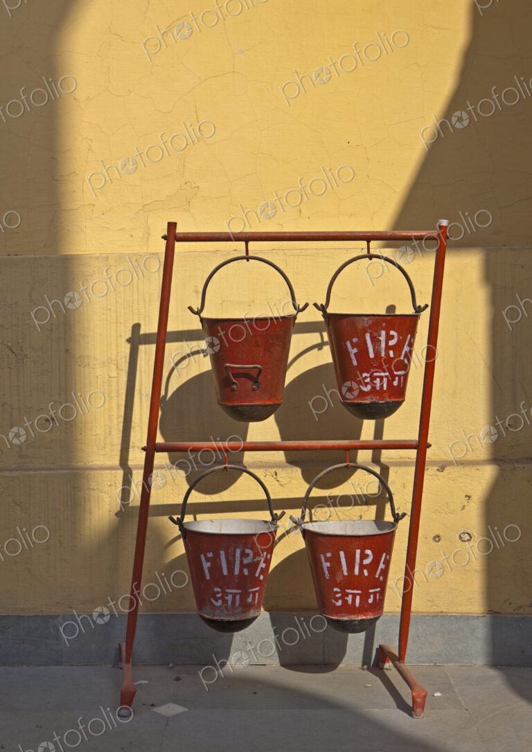 A row of red fire sand buckets on a frame outside a building, the Birla temple in New…