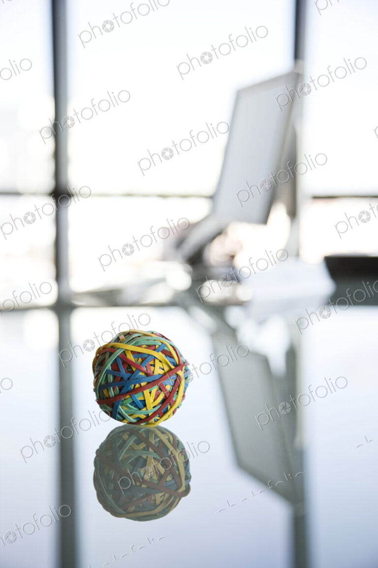 A rubber band ball sitting on a reflective desk in an office.