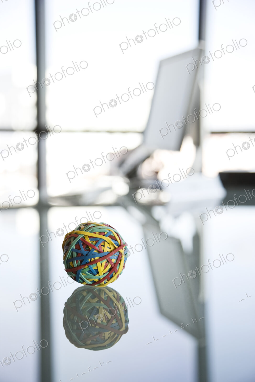 A rubber band ball sitting on a reflective desk in an office.