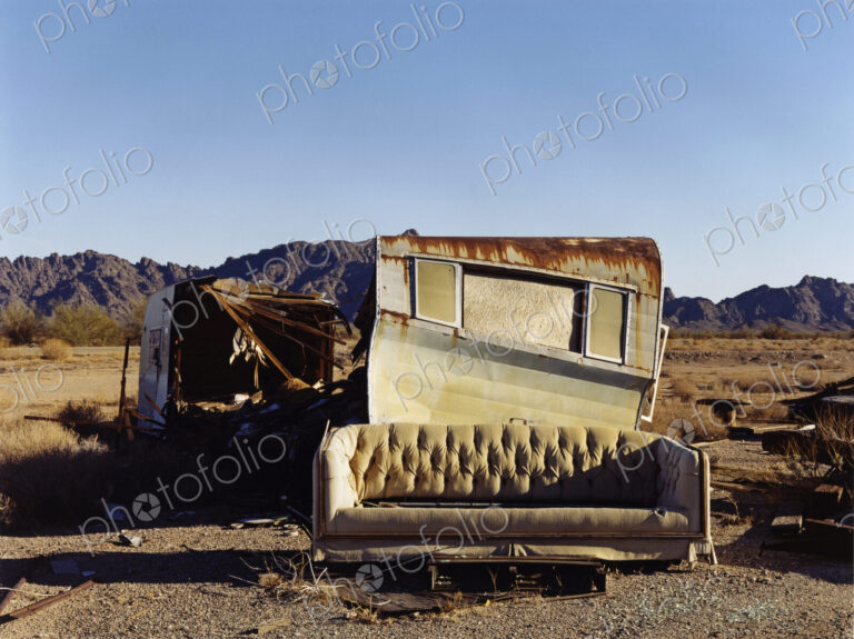 A ruined caravan, with rusting roof, a shelter, and a sofa.