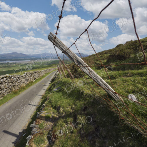 A rural hard top road and a sheep fence of wood post and barbed wire with sheep wool…