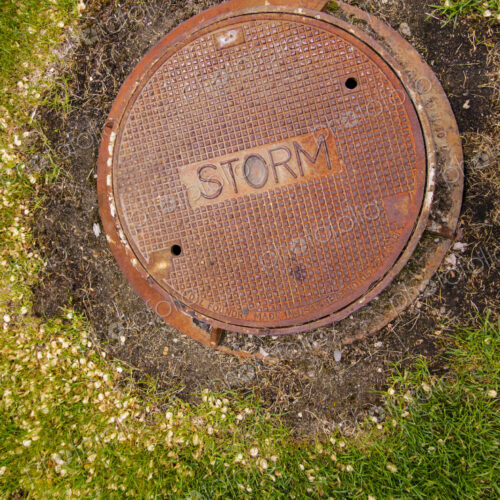 A rusting storm sewer manhole cover on a storm sewer drain. A rusting storm sewer manhole cover on a storm sewer drain.