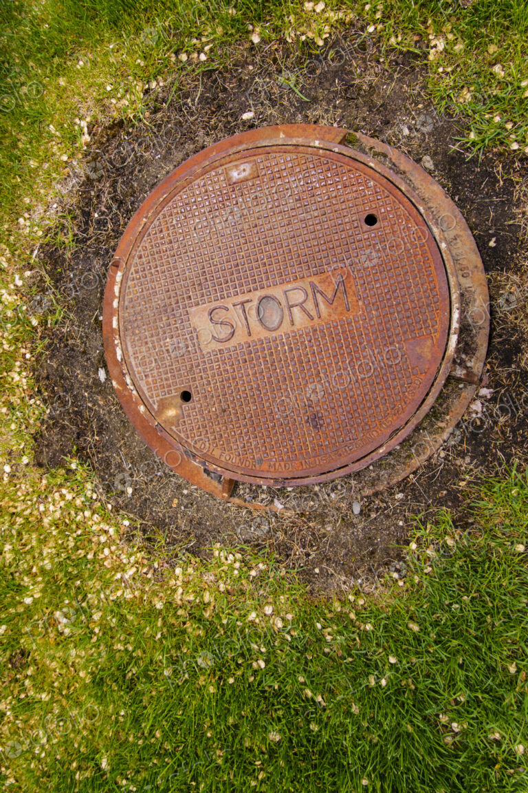 A rusting storm sewer manhole cover on a storm sewer drain.