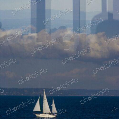 A sailboat on Puget Sound on a dark blue sea, view through a window with reflections…