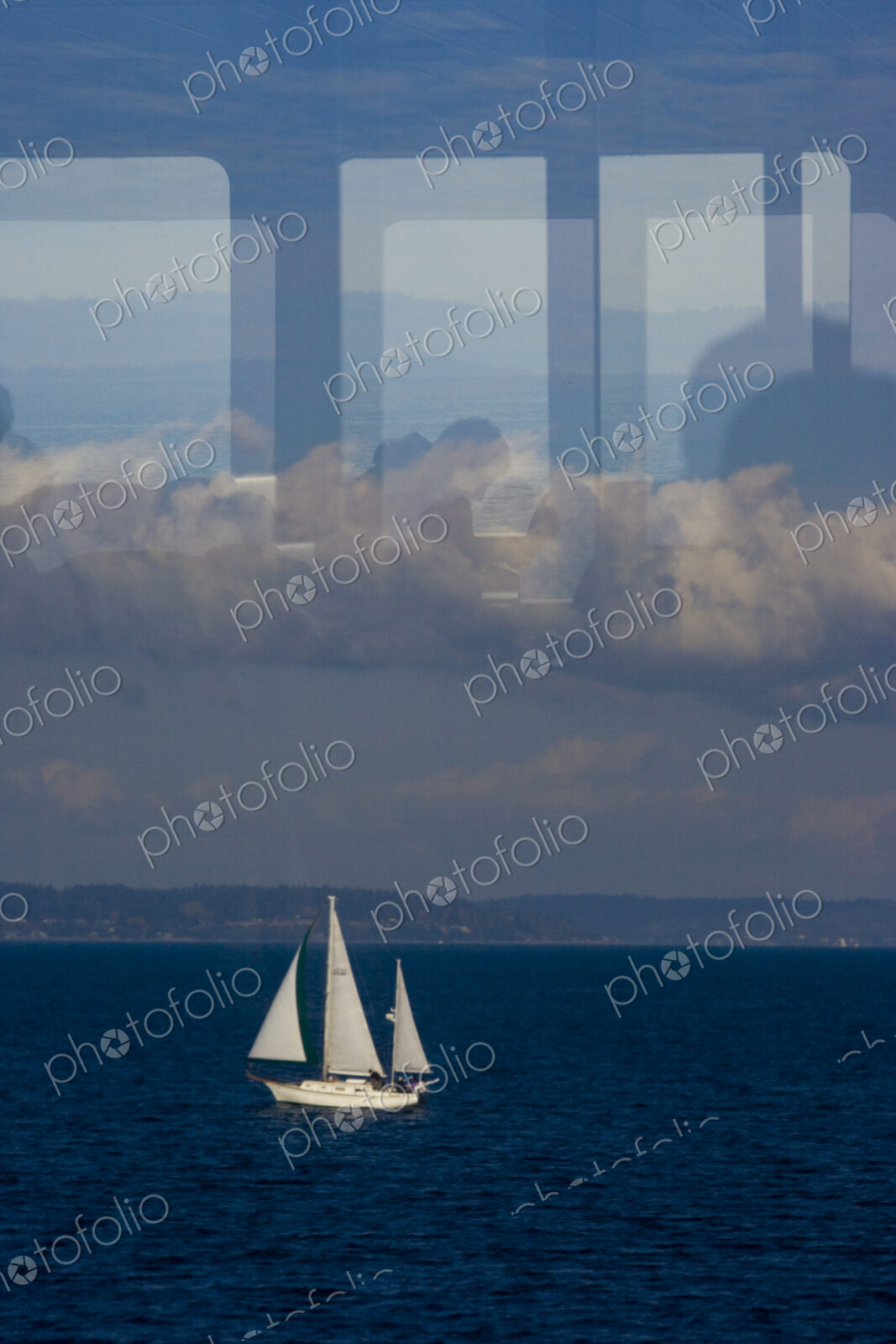 A sailboat on Puget Sound on a dark blue sea, view through a window with reflections…