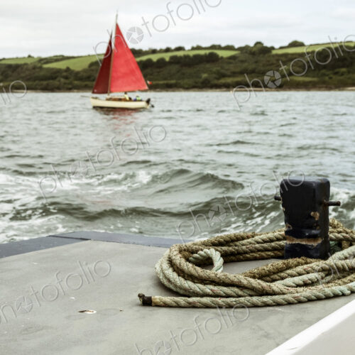 A sailing boat with bright red sails on the water, seen from another boat.