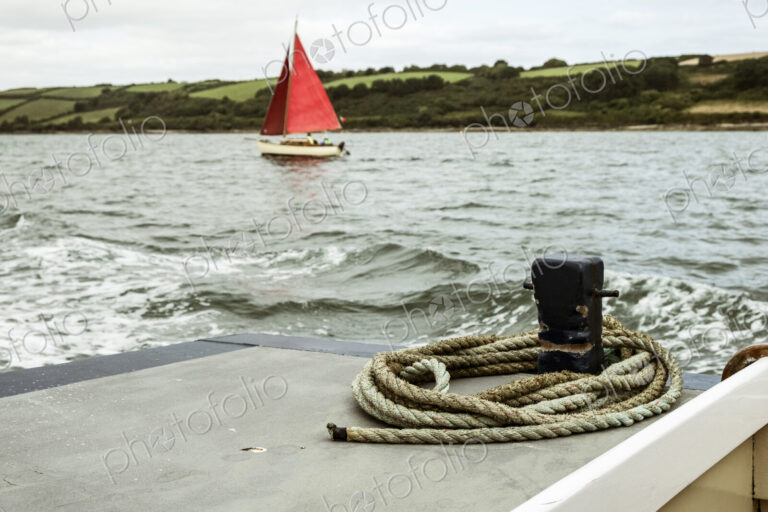A sailing boat with bright red sails on the water, seen from another boat.