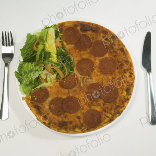 A salami pizza and salad on a plate. A salami pizza and salad on a plate.