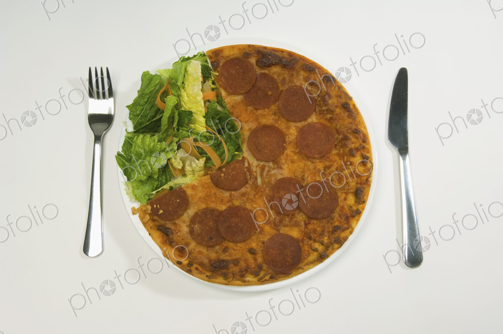 A salami pizza and salad on a plate.